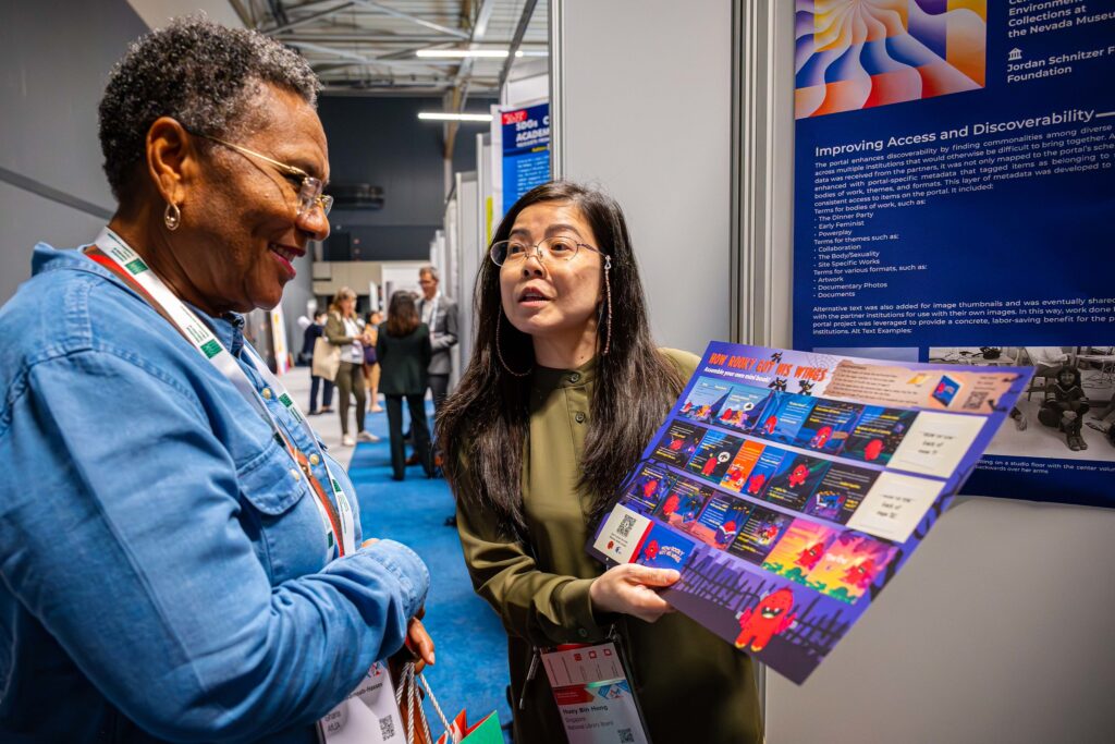 Two people engaged in conversation at a conference; one holds an illustrated poster.